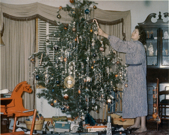 Mother playing Santa decorating Christmas tree ca. 1953